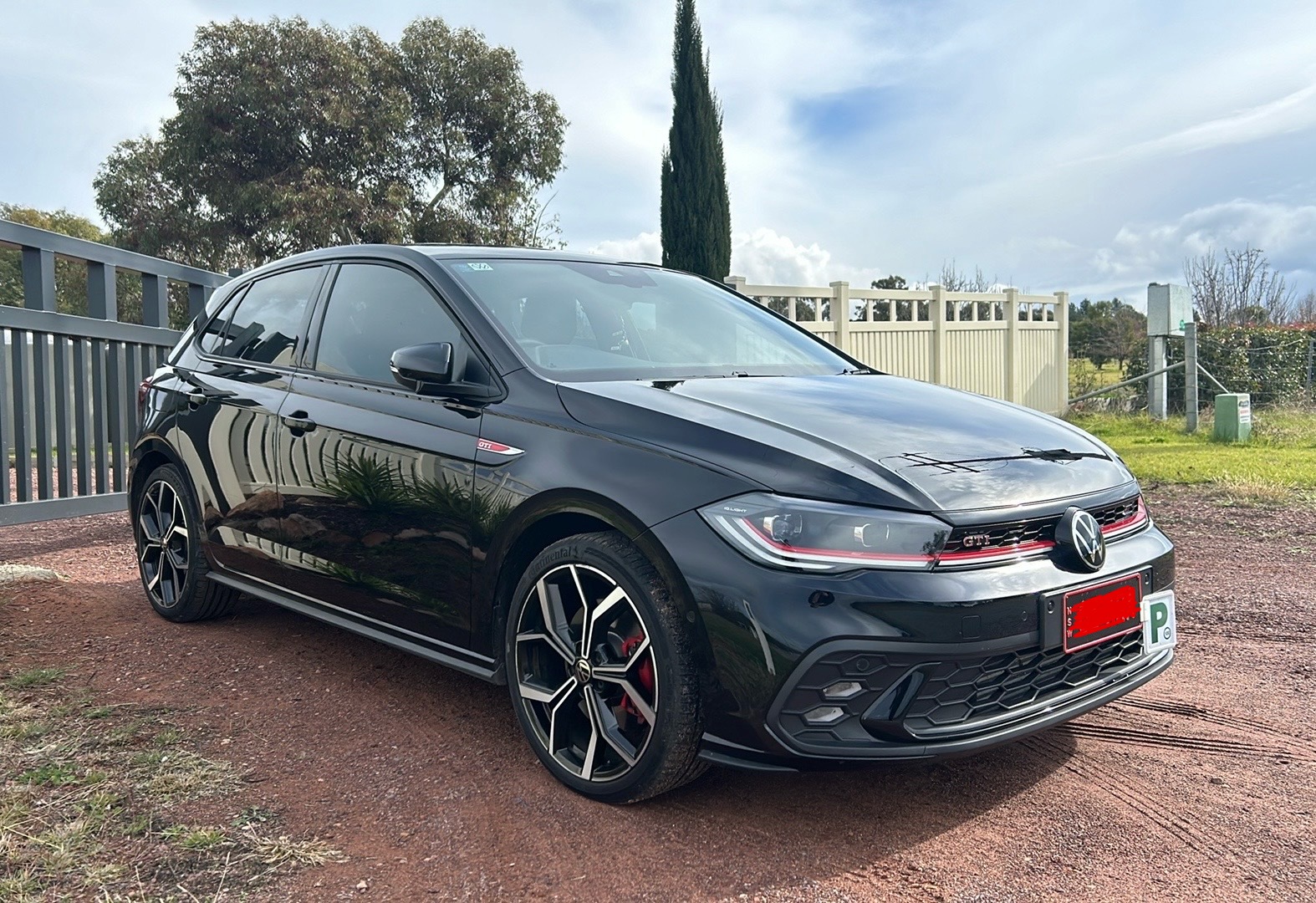 Black Volkswagen Polo GTI outside after repair, the flank reflecting the fence line cleanly