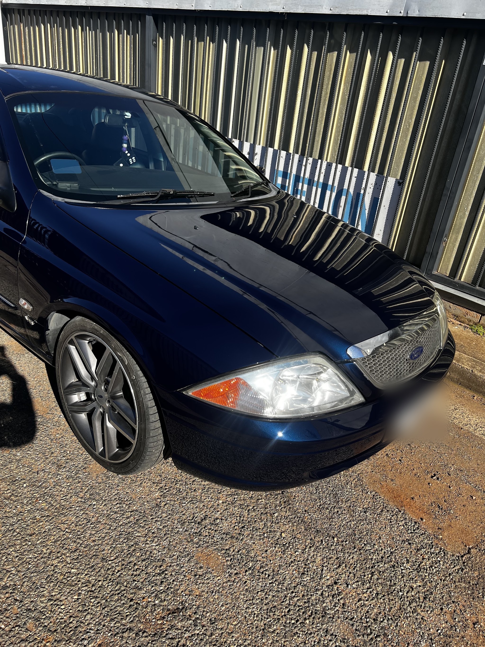 Dark blue Ford Falcon photographed front on outside the workshop, paint reflecting the shed cladding behind it