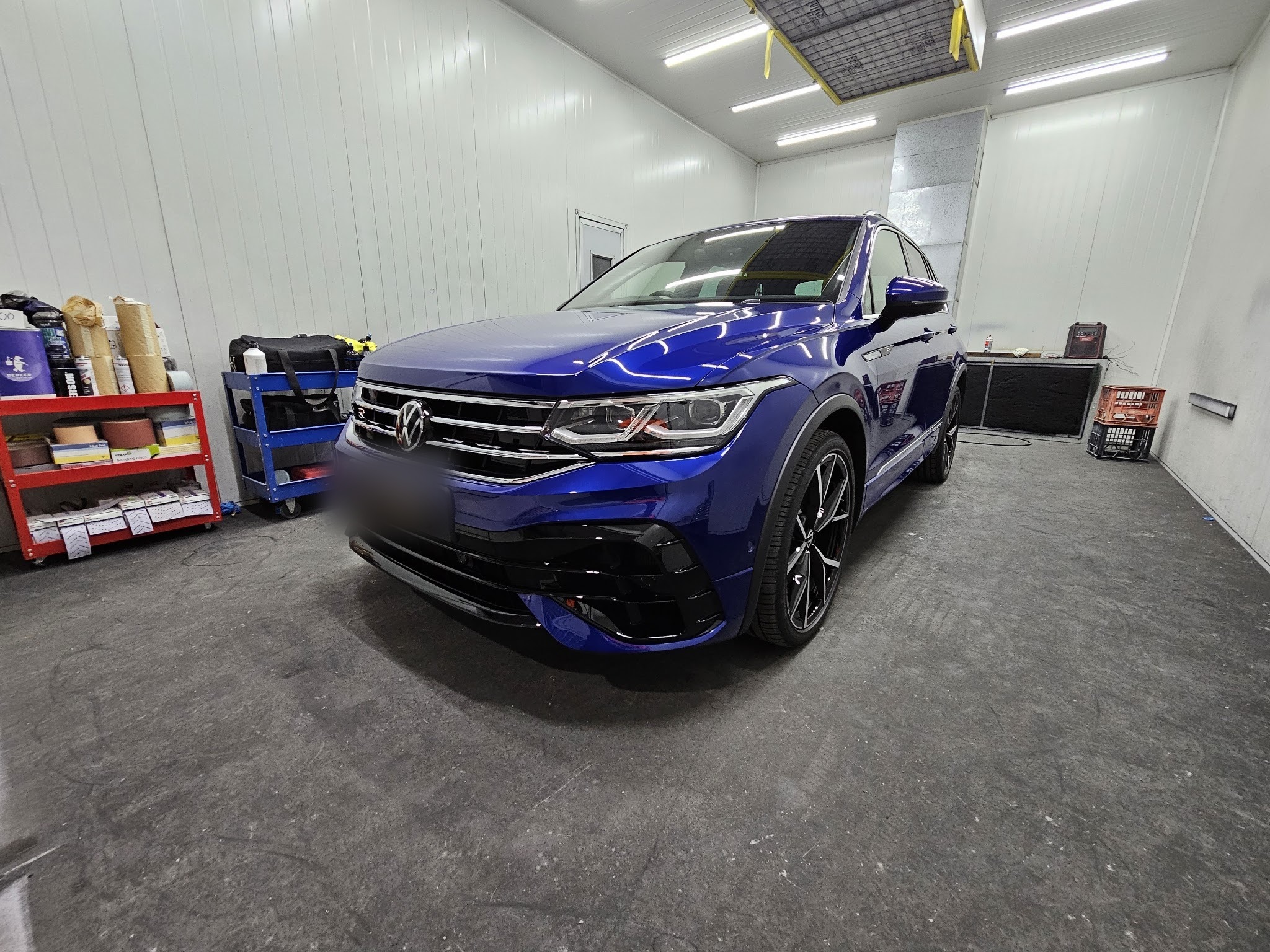 Blue Volkswagen Tiguan R inside the Bodywork Bros spray booth, prep trolleys and refinish products alongside