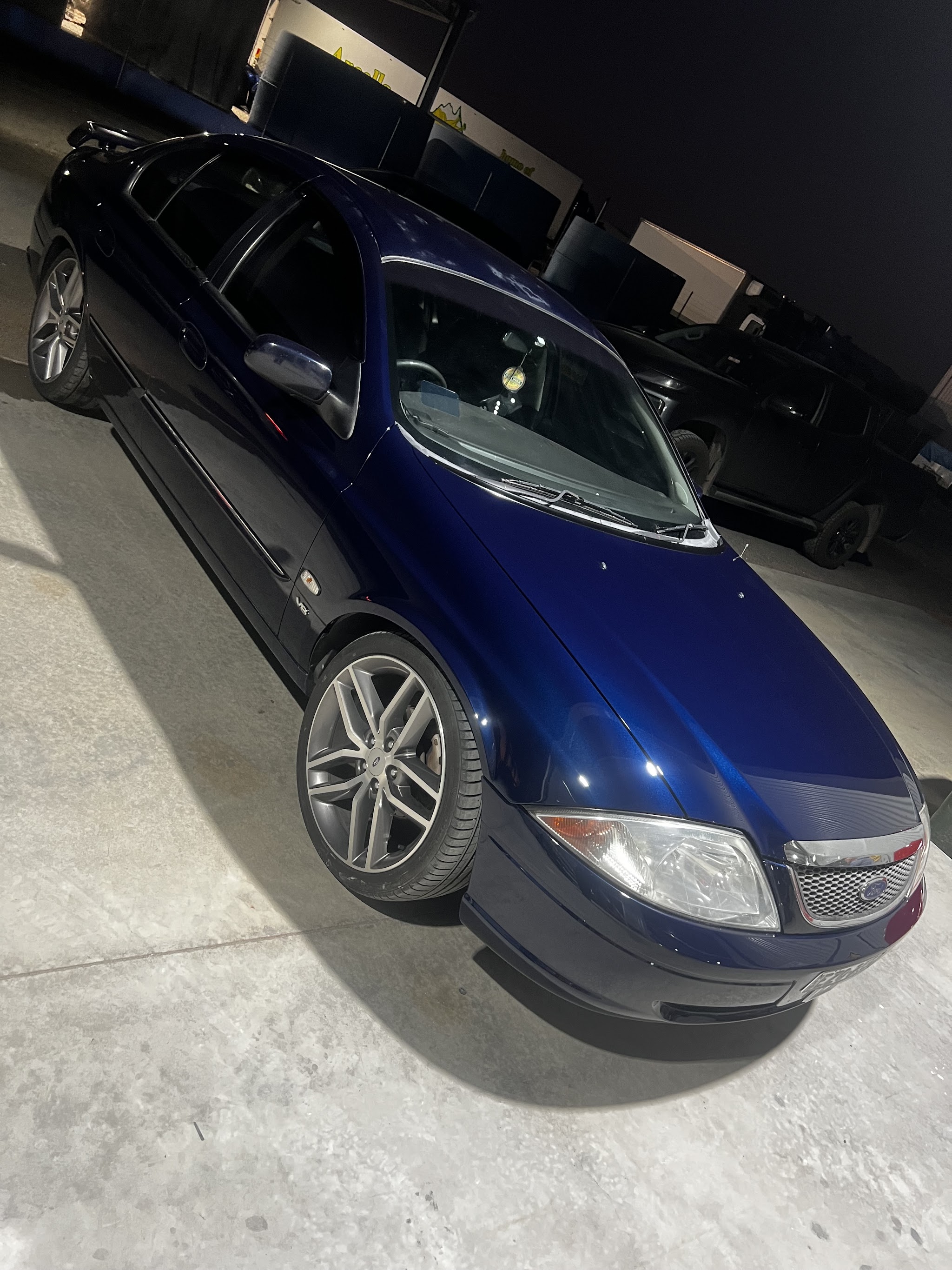 The same dark blue Falcon inside the workshop at night, deep gloss under the shop lights